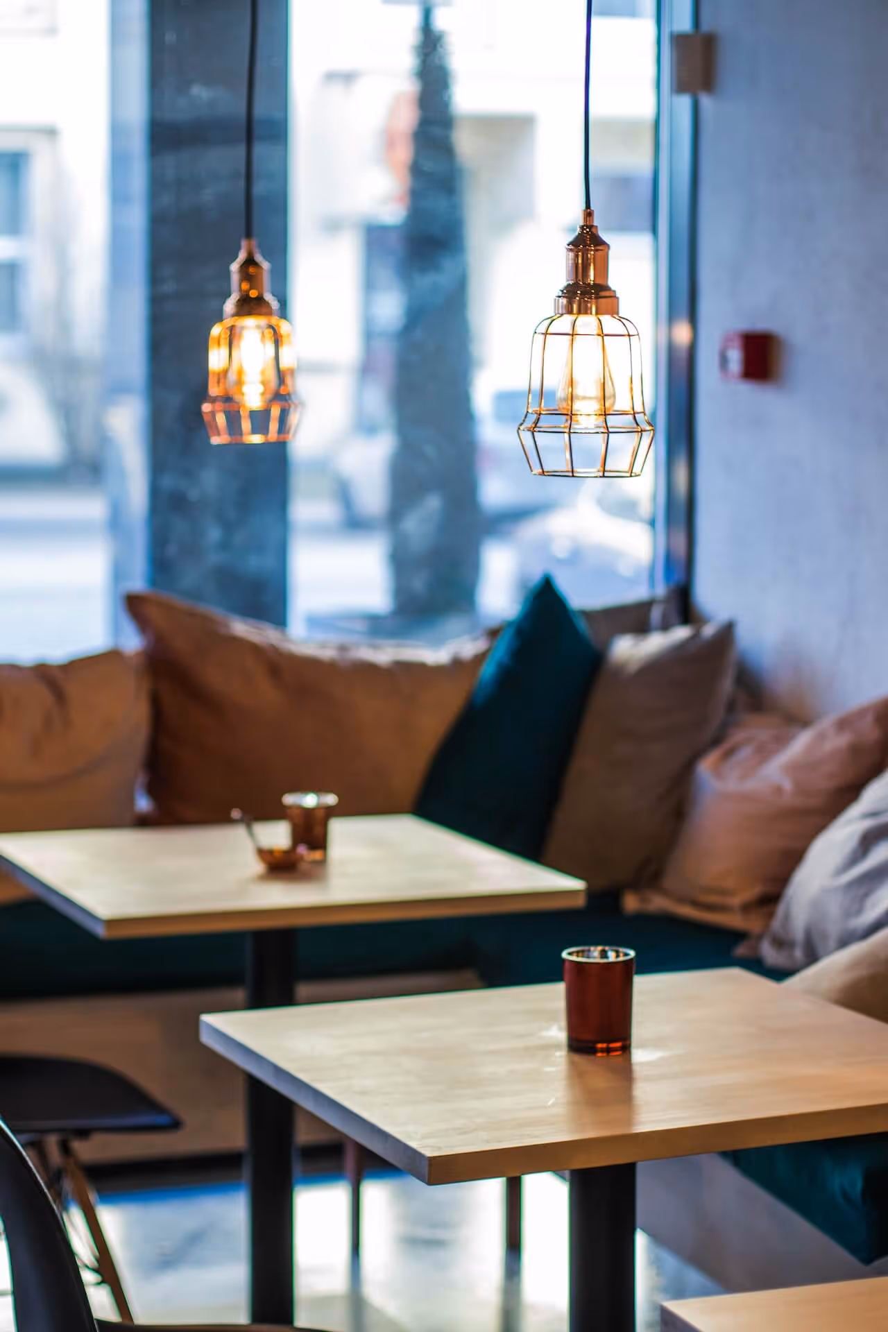 Cozy café interior with wooden tables, cushioned seating, and hanging cage pendant lights.