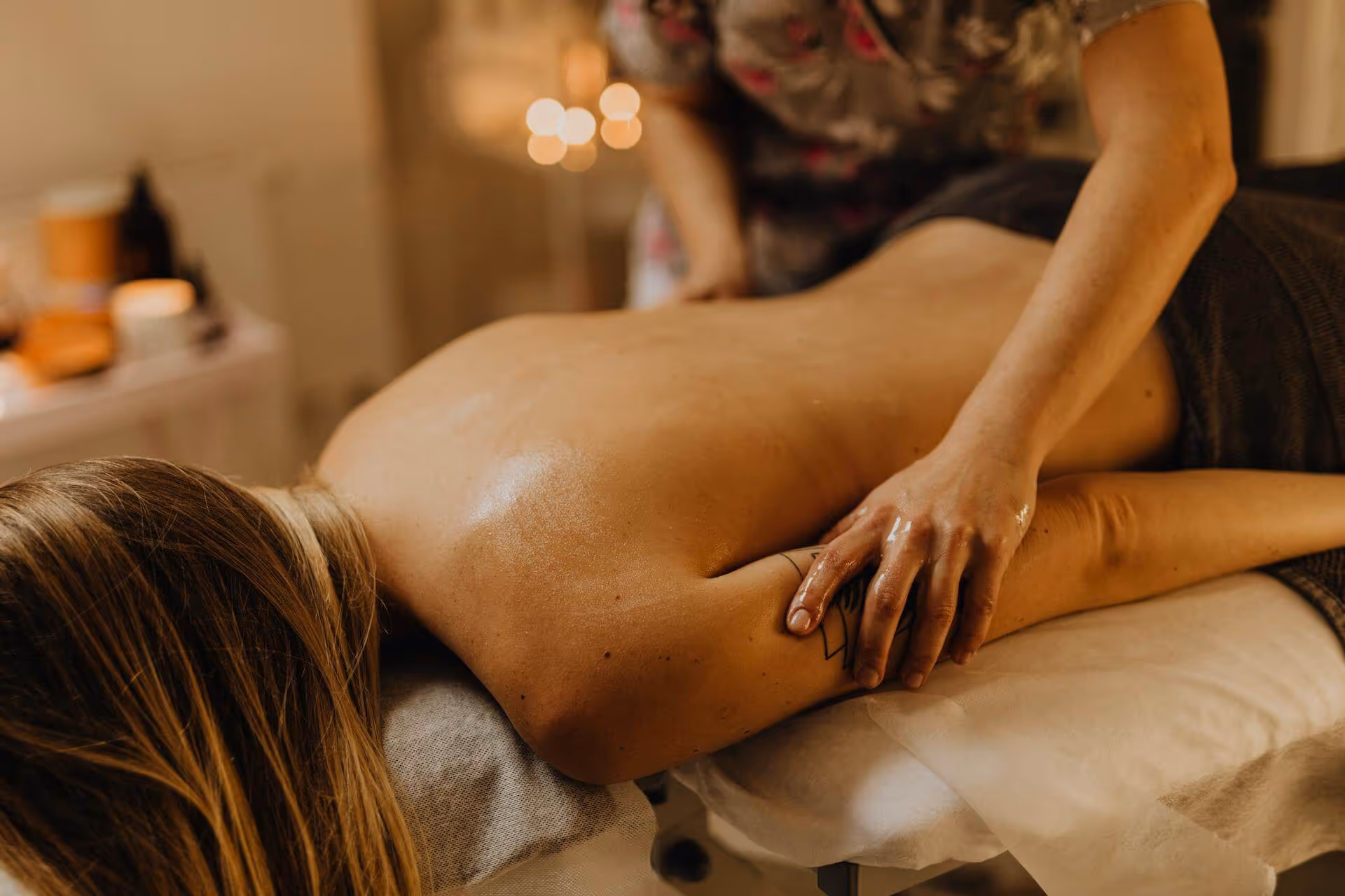 Person receiving an arm massage on a massage table in a softly lit room.