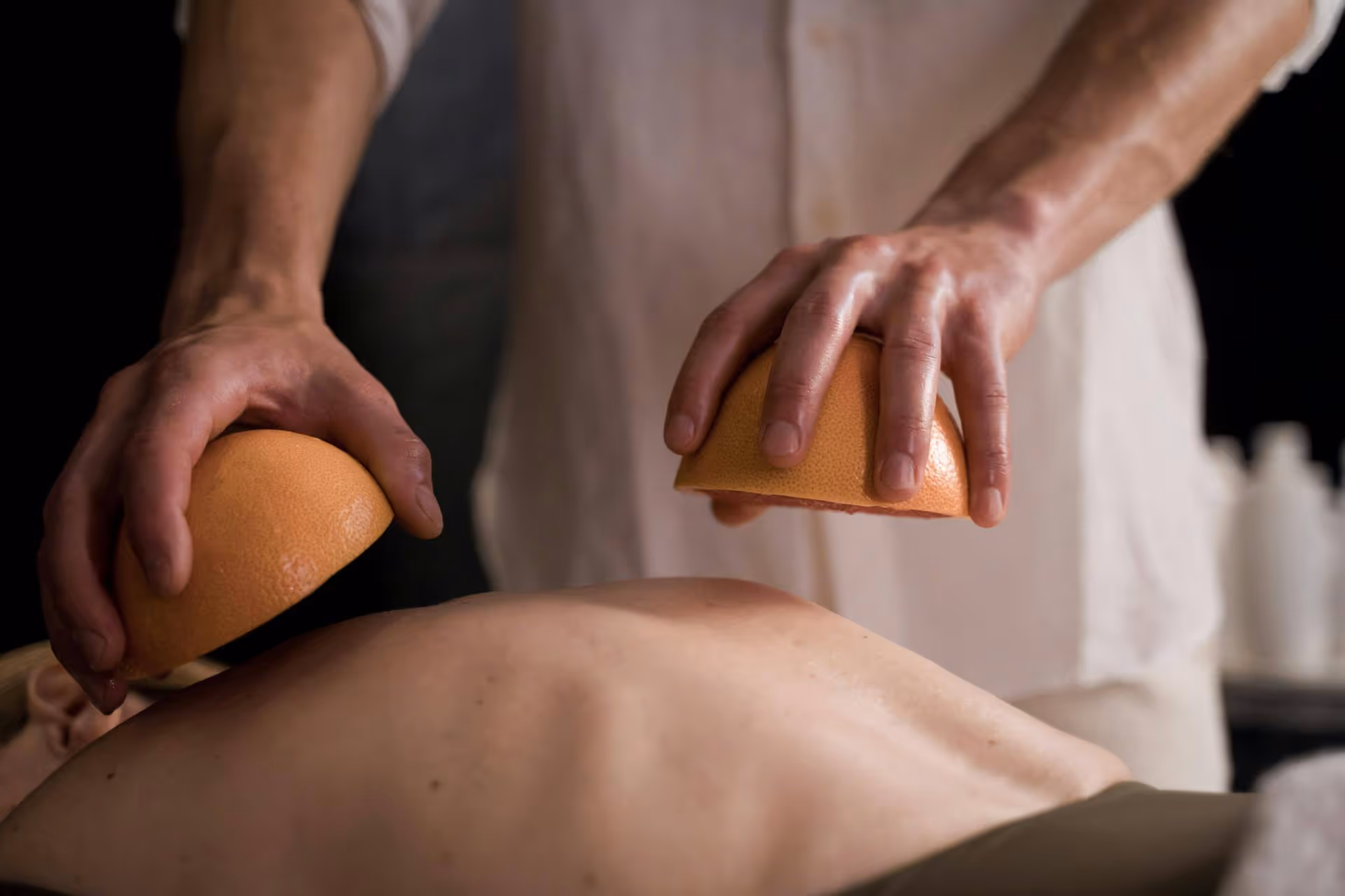 Person holding two halves of a grapefruit while massaging a bare back.