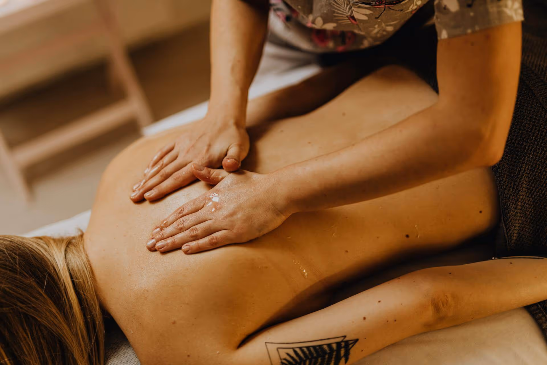 Therapist giving a back massage with oil to a person lying face down on a massage table.